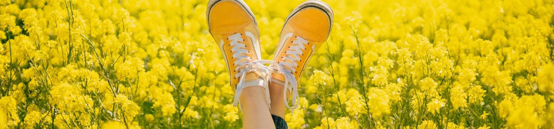 Zwei in die Luft gestreckte Füße mit gelben Sneaker vor einem gelben Rapsfeld